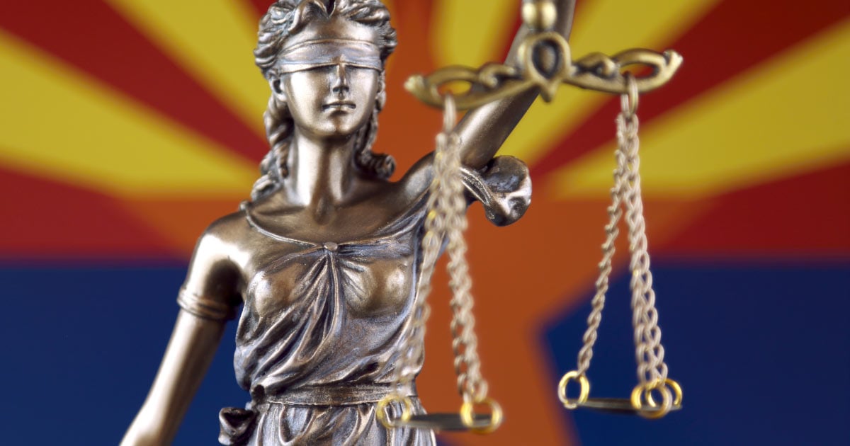Scales of justice statue in front of Arizona flag