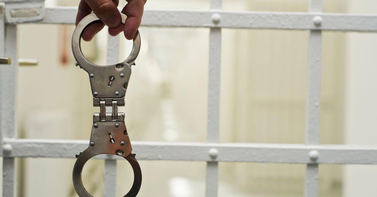 Man Holding Uncuffed Handcuffs in Front of Jail Cell