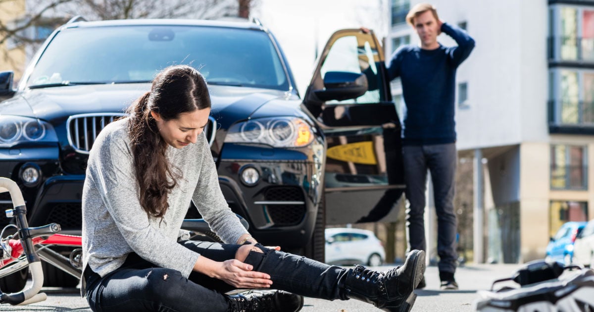 Woman holding her leg after being knocked off her bike by a car