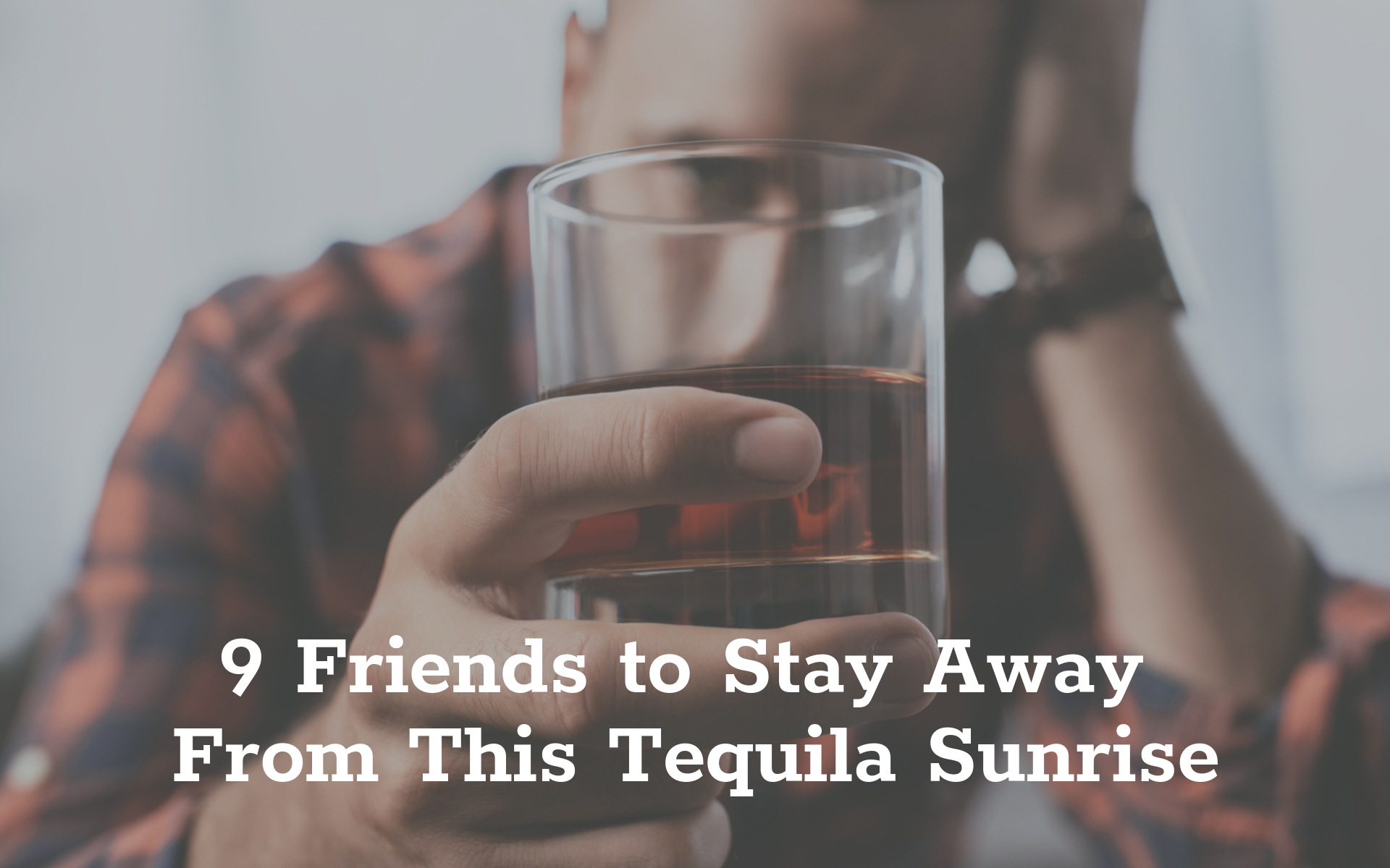 A man looking through a glass of dark liquor.