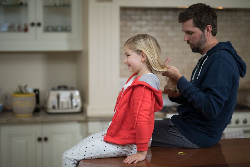 A father helps braid his daughter's hair.