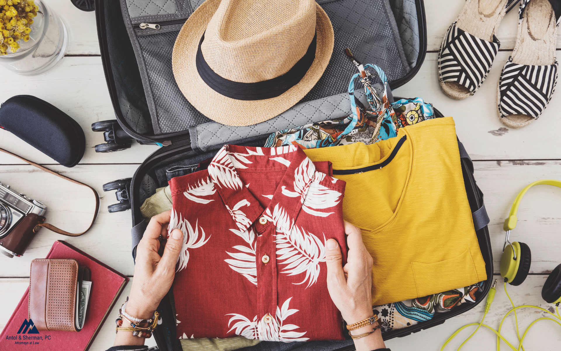 A suitcase being packed with shirts, a hat, shoes, and other travel essentials.