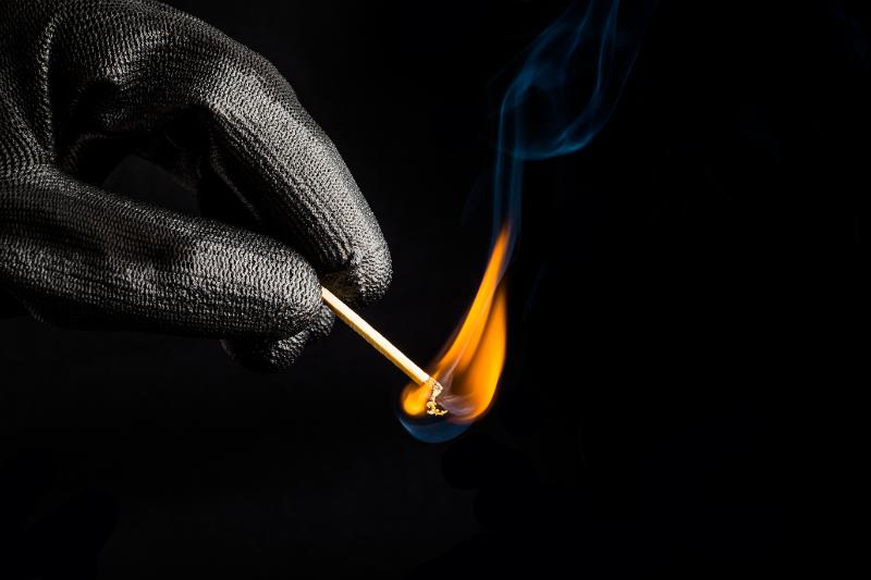 gloved fingers holding a lit match