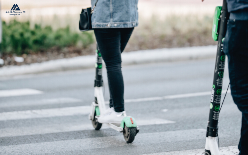 Close up of two people riding an electric scooter in a crosswalk.