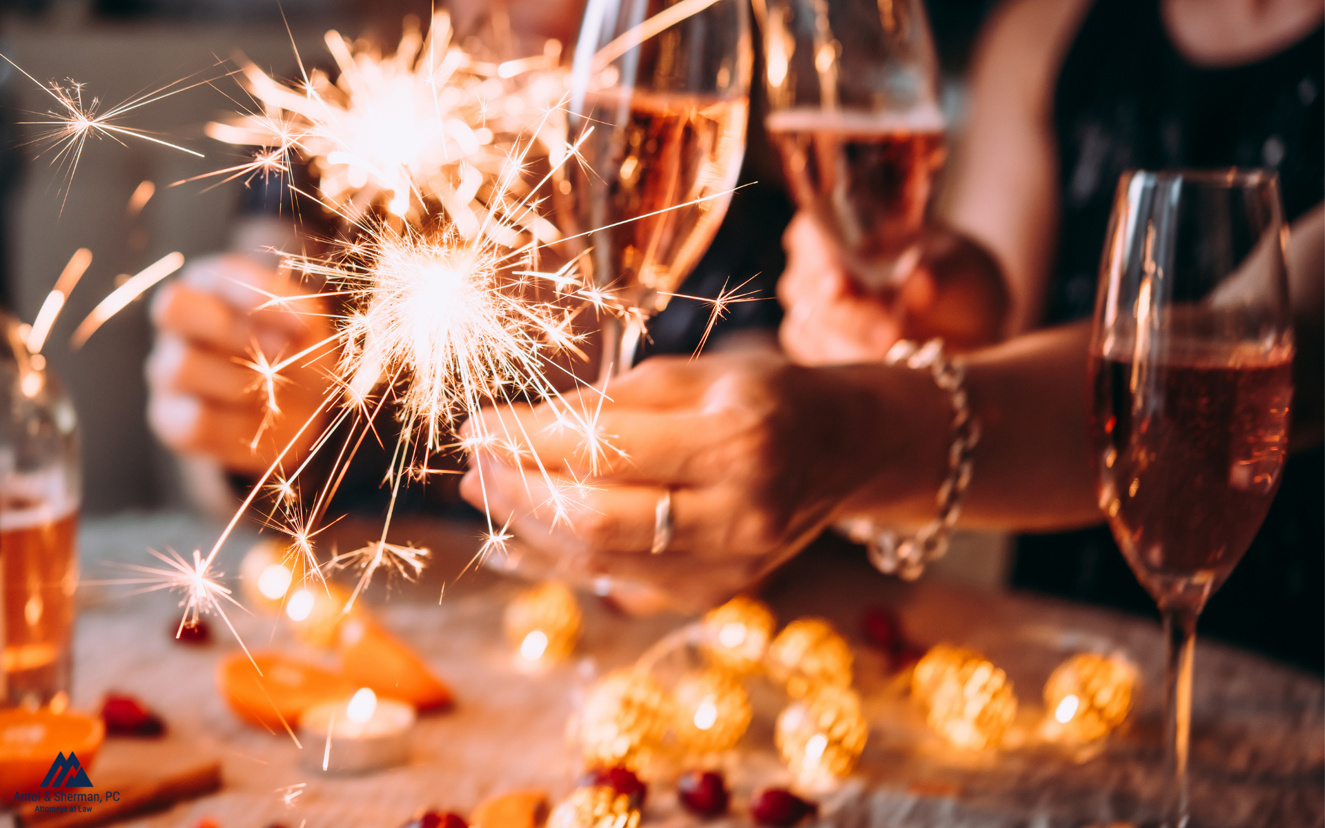 Close up of a hand holding a sparkler and other hands holding sparkling wine glasses.
