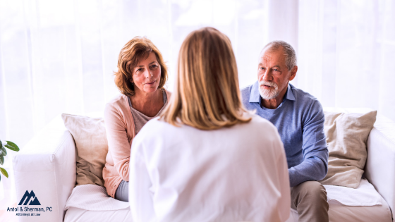 A man and woman are sitting on the couch facing forward, speaking to a woman who is sitting directly in front of them.