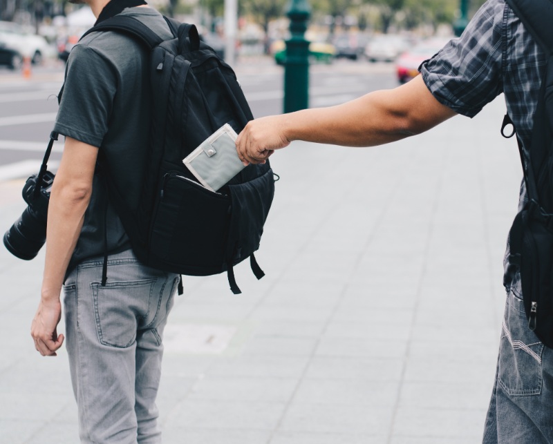 person stealing wallet from another person's backpack