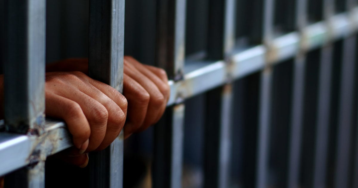 Hands holding on to prison cell bars