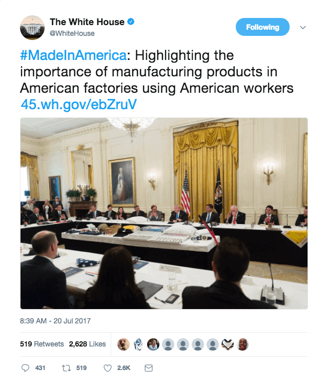 White House Tweet - Made in America Roundtable - Margarita Mendoza and Kurt Uhlir in picture 3a A large group of people in business attire sit around a long conference table at the Made in America Roundtable in the White House’s ornate East Room, with U.S. flags, documents, an American flag, and presidential seal visible amid chandeliers and gold curtains.