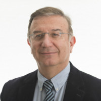 Kurt Uhlir, a middle-aged man with short, light brown hair, glasses, and a slight smile, is dressed in a navy blazer, light blue collared shirt, and striped tie. He poses against a plain, light background.