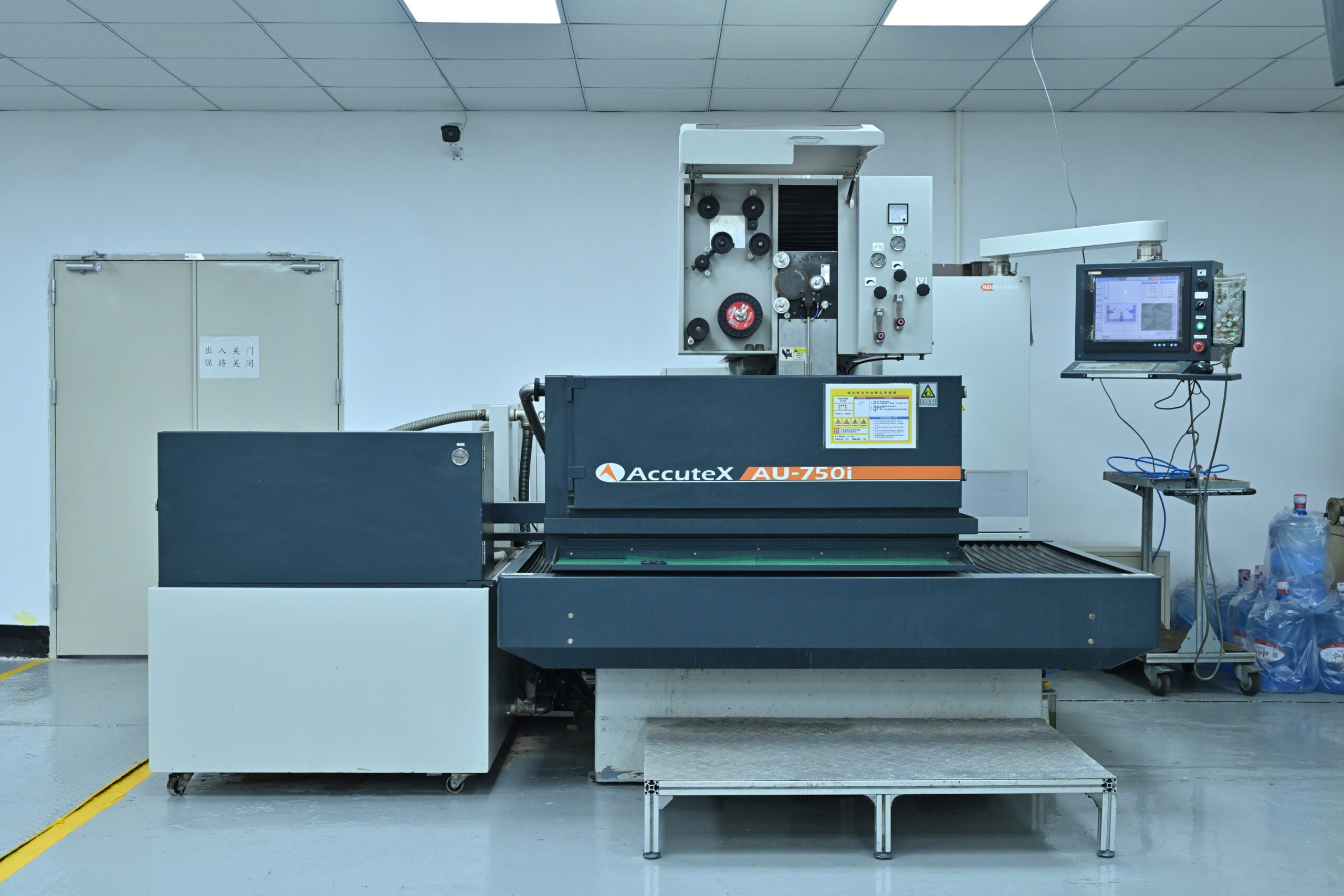 A large AccuteX AU-750i industrial machine stands in a clean, well-lit room with a control panel and monitor on the right side.