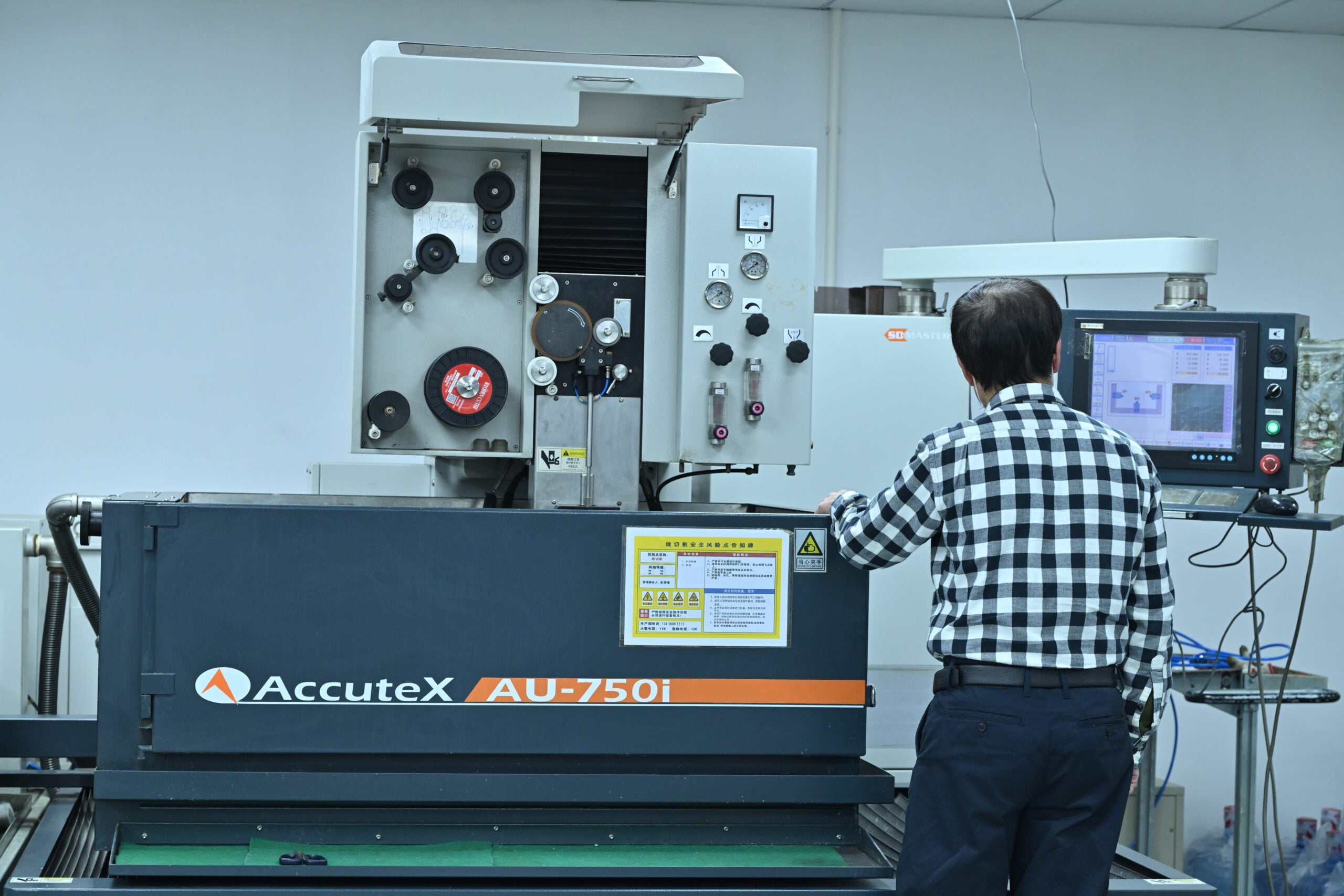 A person operates an AccuteX AU-750i industrial machine, monitoring data on a control panel in a factory setting.