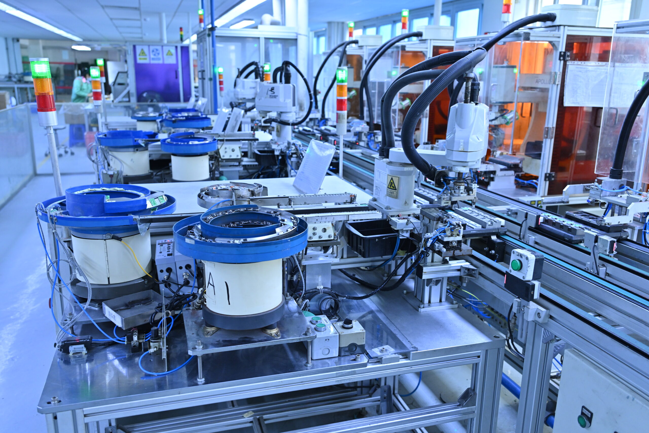 Automated machinery and robotic arms operate on an assembly line in a bright, modern manufacturing facility.