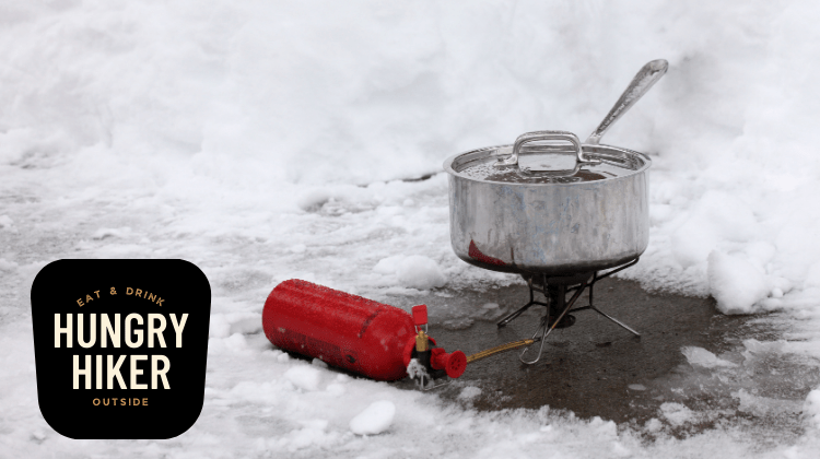 This photo shows a liquid-fuel backpacking stove in use in the snow.