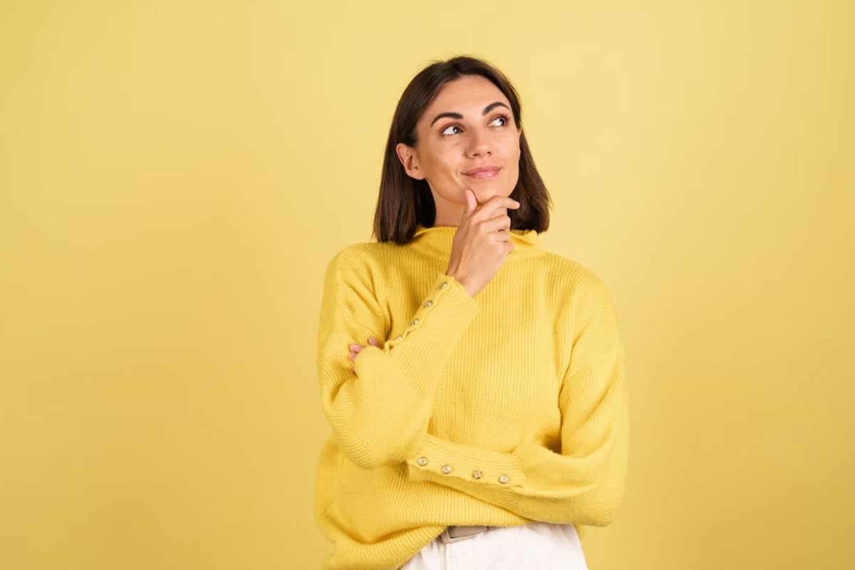 mujer joven pensativa con un suéter amarillo.