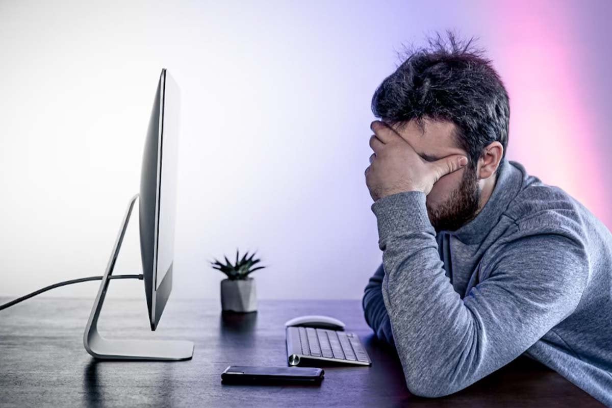 Un hombre está sentado en un escritorio con la mano en la cabeza, analizando la frecuencia y las métricas de los anuncios de Facebook.