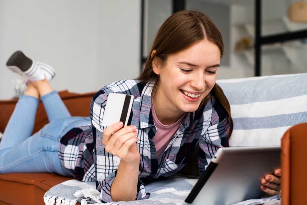 Una mujer joven en un sofá que hace compras en línea con una computadora portátil y una tarjeta de crédito a través de la página de inicio de conversiones.
