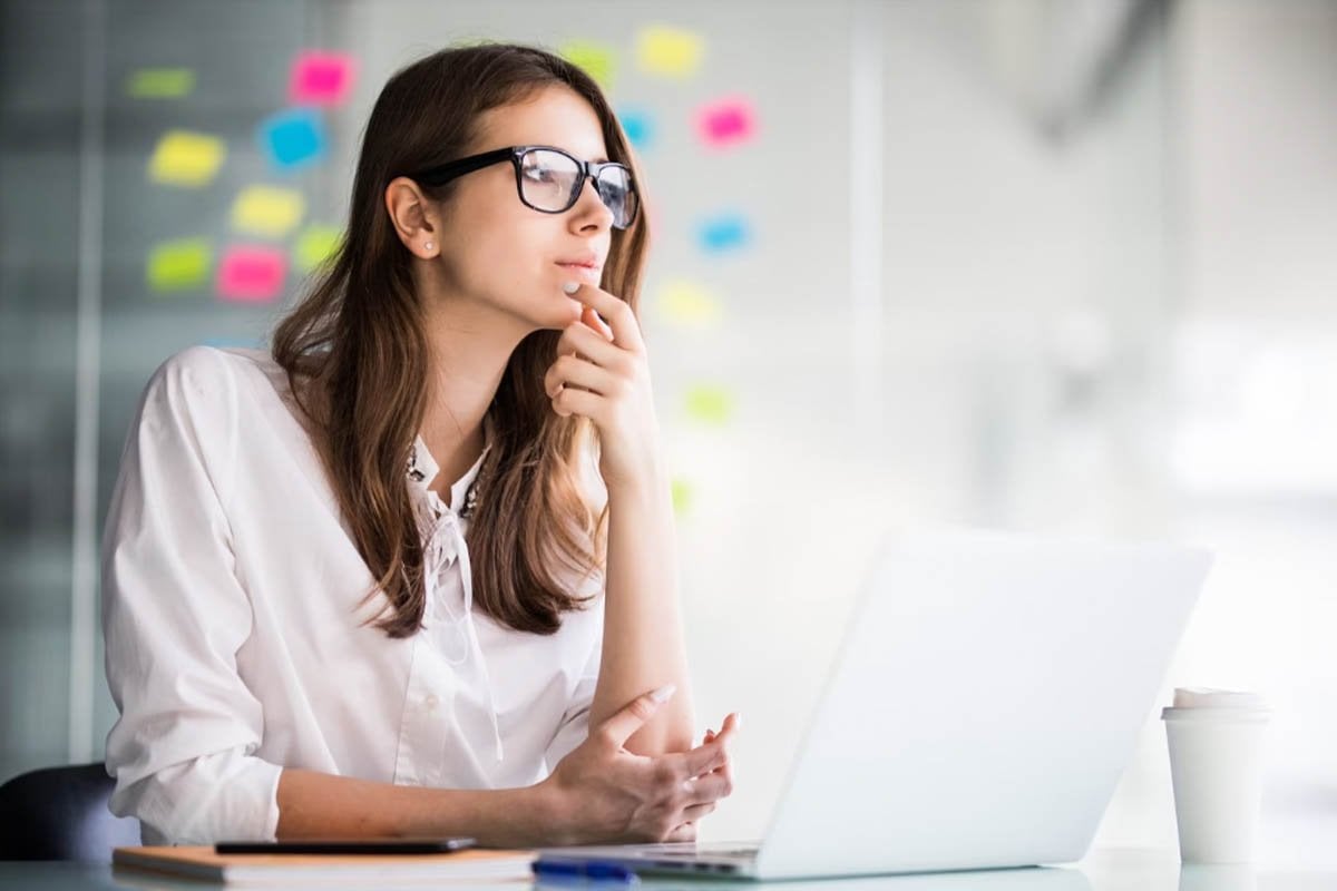 Una mujer está sentada frente a una computadora portátil usando gafas.
