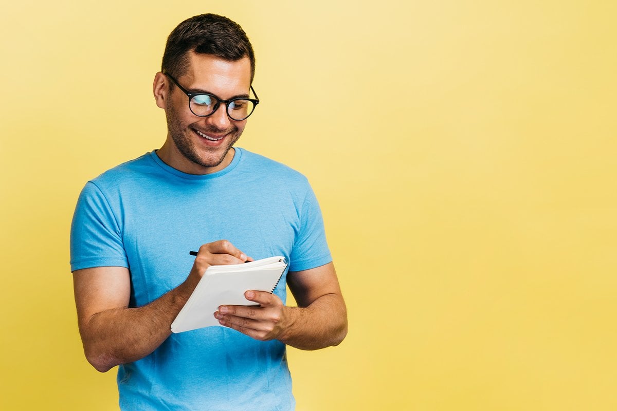 Un hombre que lleva gafas redacta un portapapeles sobre un fondo amarillo.