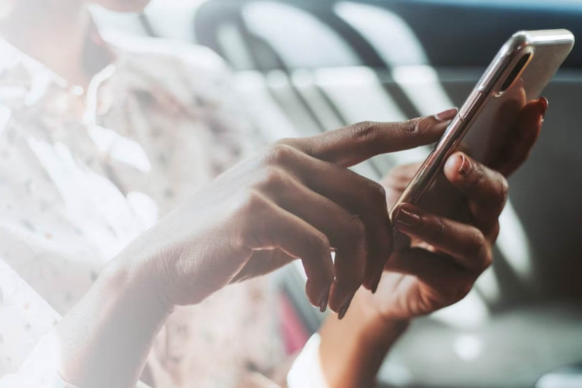 Una mujer está usando un teléfono celular mientras chatea en Facebook.