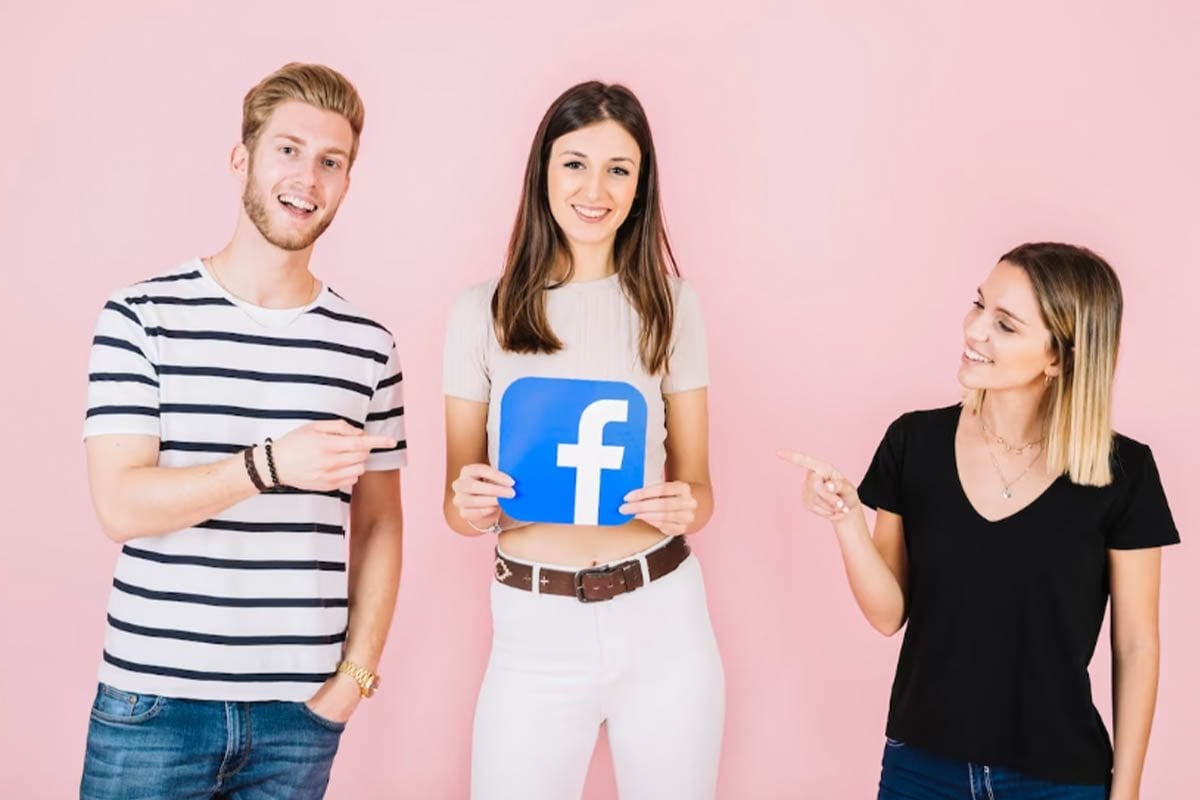 Tres personas mostrando un letrero de Facebook contra un fondo rosa vibrante.