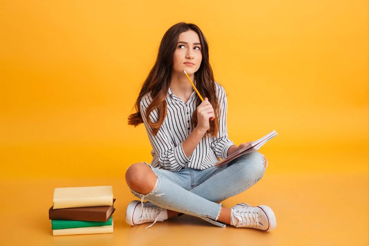 Una chica que usa Google Ads sentada en el suelo con libros y un lápiz.