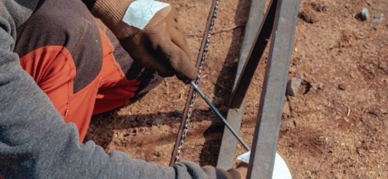 man sharpening a chainsaw blade with gloves on