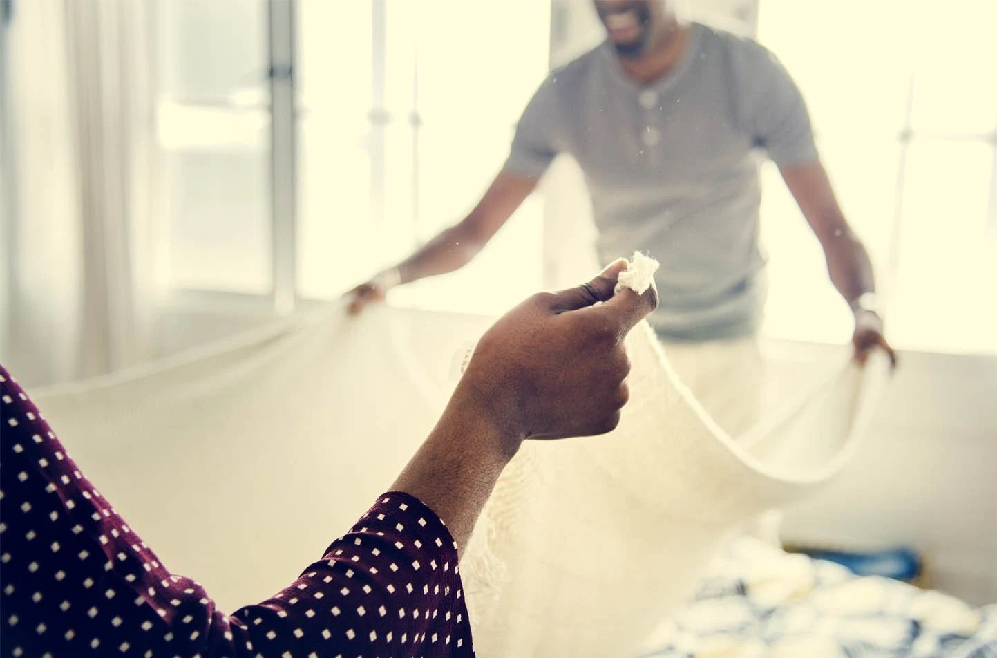 black couple changing bed sheets together to spring clean their home