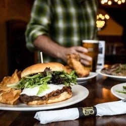 table with burger & chips, napkin & man holding beer