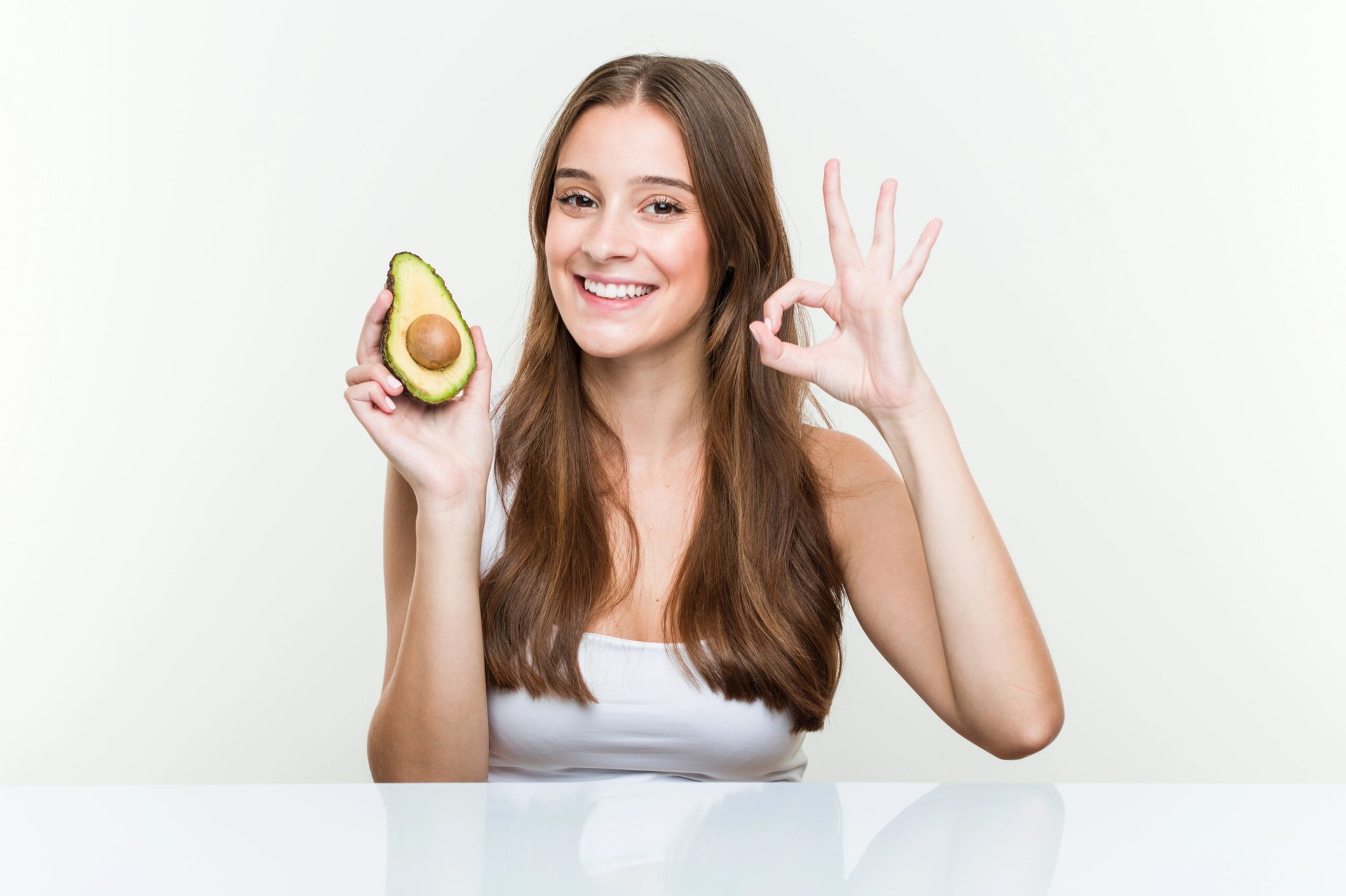 Femme souriante montrant un avocat et signe OK.