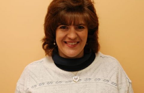Woman with a smile wearing a white sweater with a navy collar and a heart-shaped pendant. Woman with a smile wearing a white sweater with a navy collar and a heart-shaped pendant.