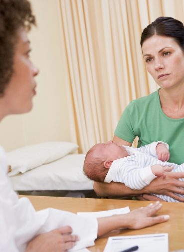 A mother holding her baby during a consultation with a healthcare professional. A mother holding her baby during a consultation with a healthcare professional.
