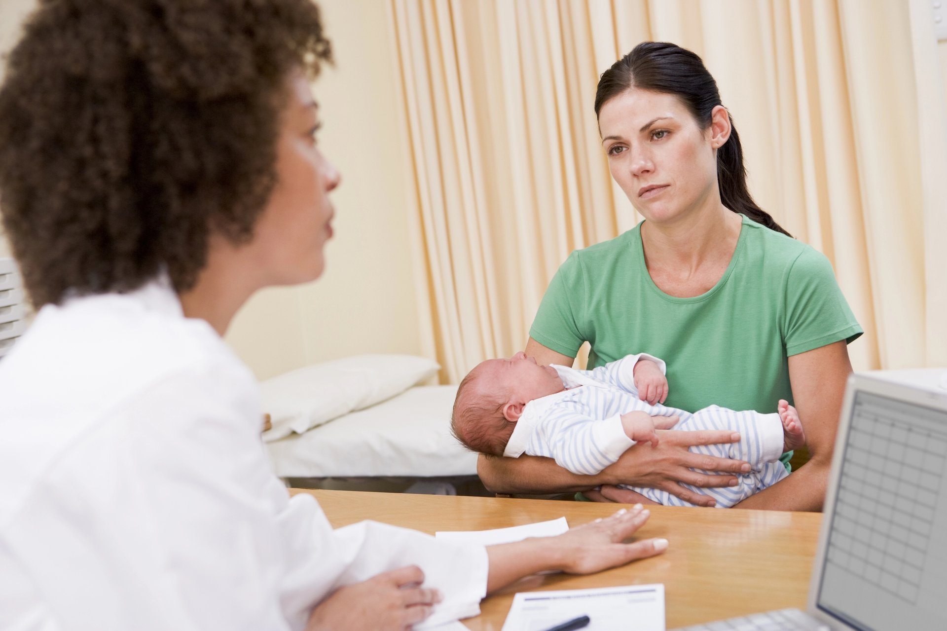 A mother holding her baby during a consultation with a healthcare professional.