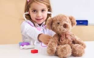 A young girl plays pretend doctor with a stethoscope and a teddy bear. A young girl plays pretend doctor with a stethoscope and a teddy bear.
