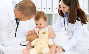 Two pediatricians interacting with a baby patient holding a stuffed toy. Two pediatricians interacting with a baby patient holding a stuffed toy.