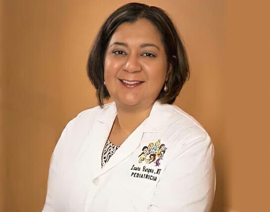 A professional portrait of a smiling pediatrician wearing a white lab coat with an embroidered name and title.