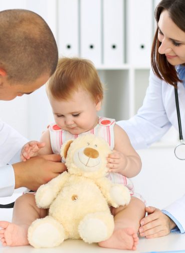 Two pediatricians interacting with a baby patient holding a stuffed toy. Two pediatricians interacting with a baby patient holding a stuffed toy.