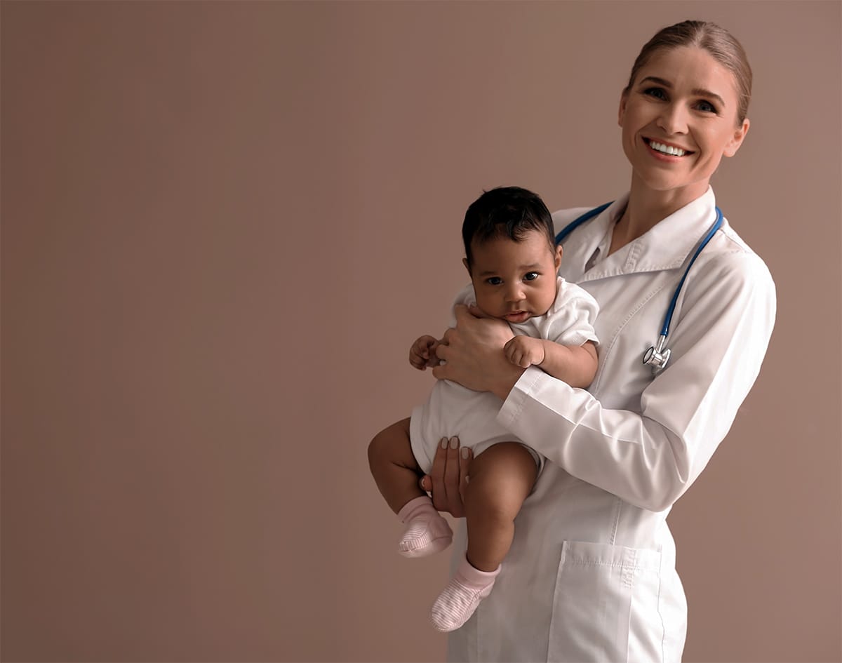 A smiling healthcare professional holding a baby with care and confidence against a neutral background. A smiling healthcare professional holding a baby with care and confidence against a neutral background.