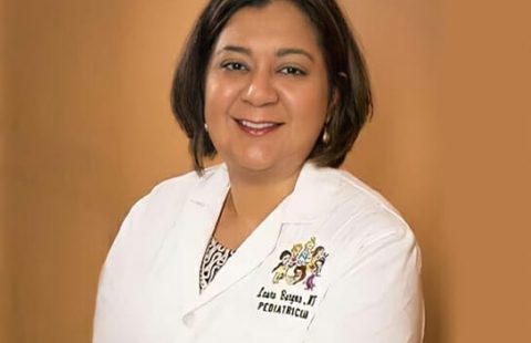 A professional portrait of a smiling pediatrician wearing a white lab coat with an embroidered name and title. A professional portrait of a smiling pediatrician wearing a white lab coat with an embroidered name and title.