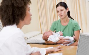 A mother holding her baby during a consultation with a healthcare professional. A mother holding her baby during a consultation with a healthcare professional.