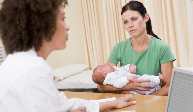 A mother holding her baby during a consultation with a healthcare professional. A mother holding her baby during a consultation with a healthcare professional.