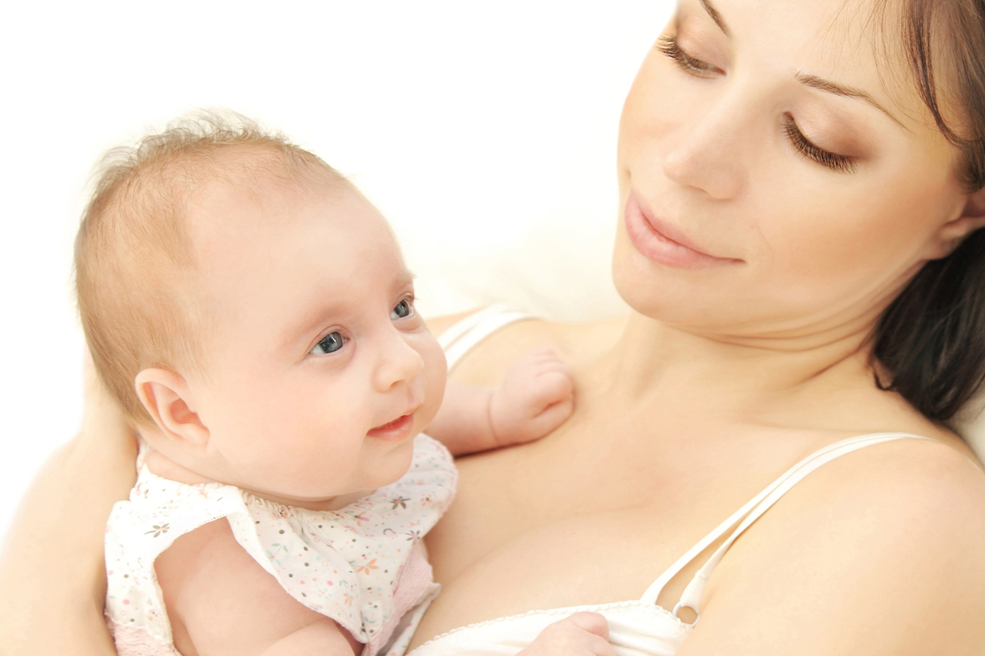 A woman gazes lovingly at the baby in her arms, who looks upwards with a curious expression. They are both bathed in soft, natural light.