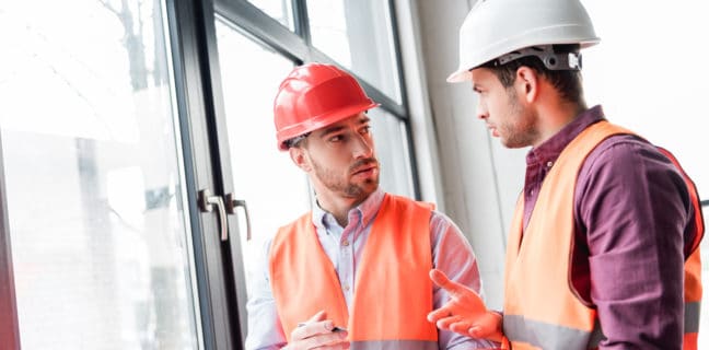 Jetzt den Gasverbrauch senken fireman in helmet looking at coworker while talking and holding red extinguisher
