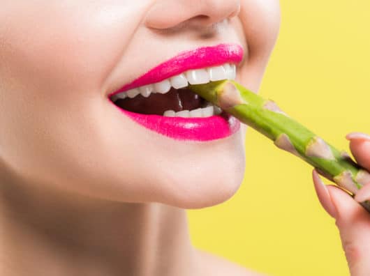 Spargel – lecker und gesund – Spargelsaison eröffnet cheerful woman holding green and tasty asparagus in mouth isolated on yellow