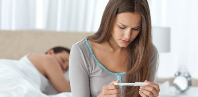 What It Feels Like to Want Children: Ten Real-Life Stories Pretty woman looking a pregnancy test while her boyfriend sleepi