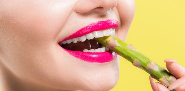 Spargel – lecker und gesund – Spargelsaison eröffnet cheerful woman holding green and tasty asparagus in mouth isolated on yellow
