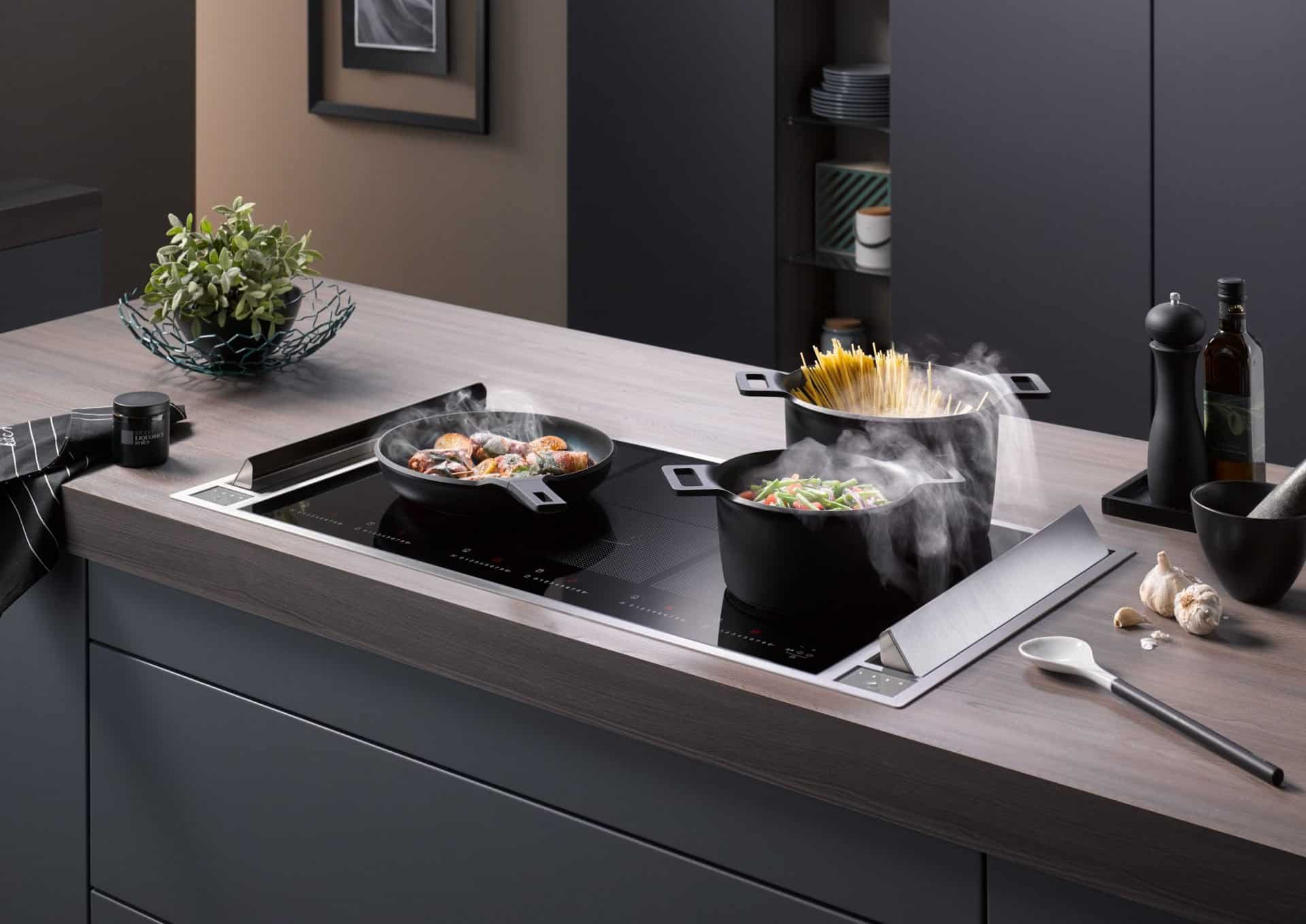 Insbesondere für Kochinseln eignen sich Dunstabzüge, die in die Arbeitsfläche integriert sind. Im Betrieb öffnen sich die Klappen, sodass Kochdünste unmittelbar dort abgesaugt werden, wo sie entstehen. Bildquelle: tdx/Homeier