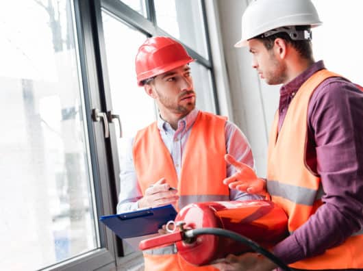 Jetzt den Gasverbrauch senken fireman in helmet looking at coworker while talking and holding red extinguisher