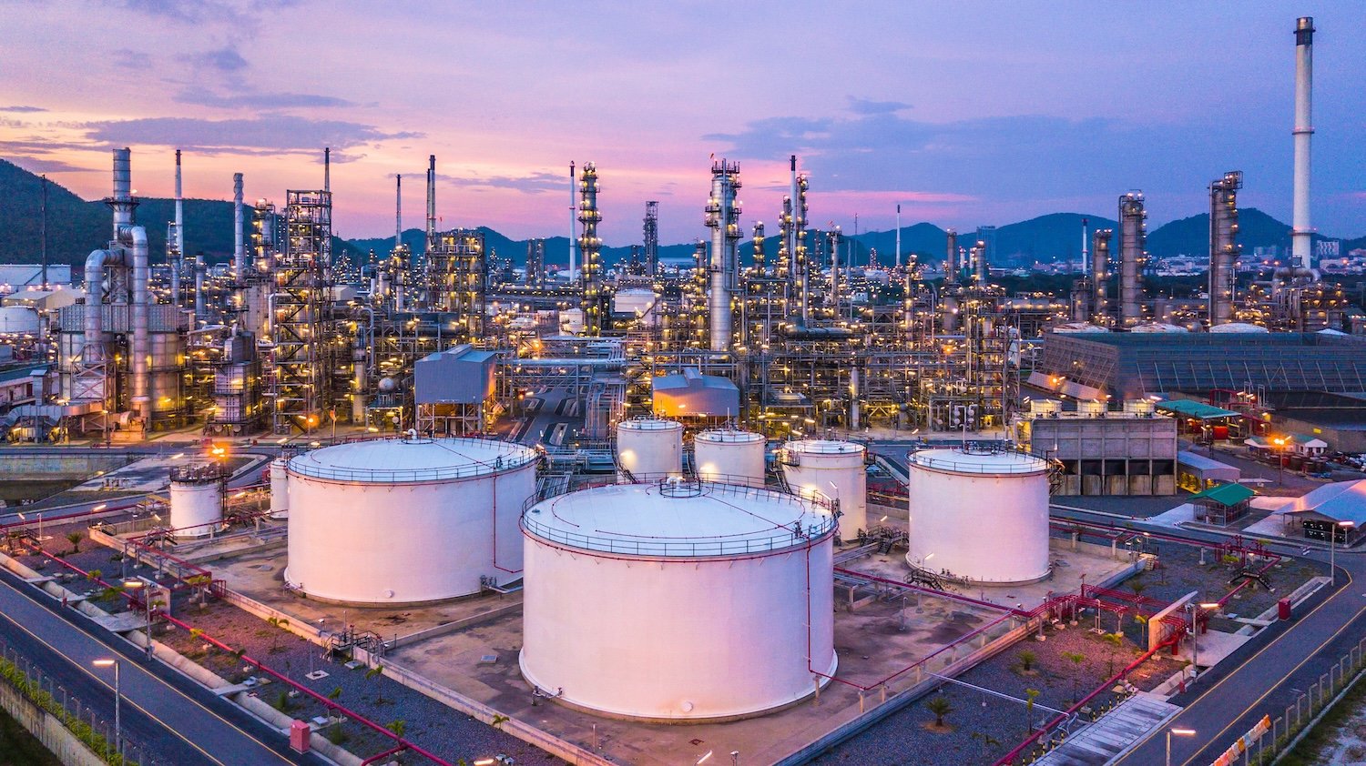 Aerial top view oil and gas chemical tank with oil refinery plant background at twilight.