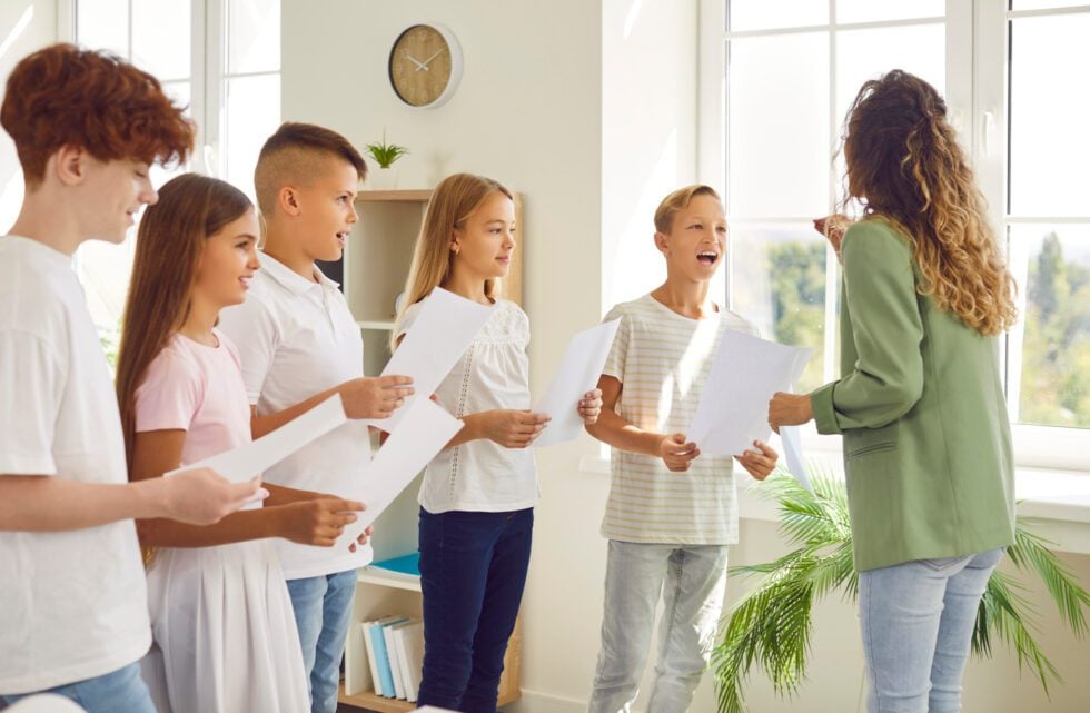 Young school children standing in a circle with their young female teacher having music lesson